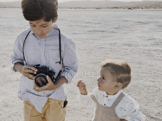 Un niño sostiene una cámara y un niño más joven está a mi lado. - foto de stock