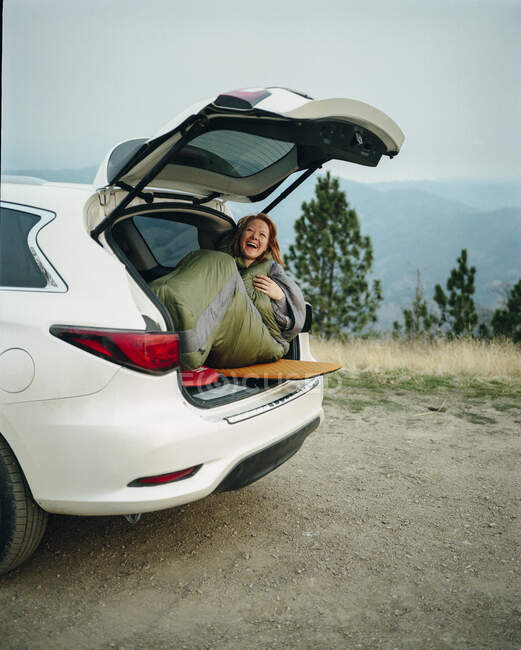 Woman in sleeping bag laughing while car camping in Big Sur — Stock Photo