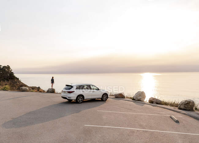 Una macchina parcheggiata al Big Sur Punto di vista con donna in piedi sulla roccia — Foto stock