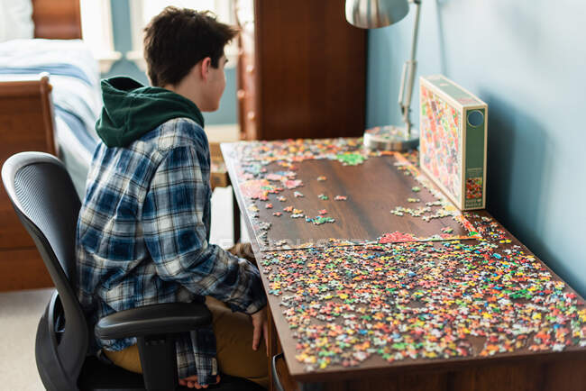 Teenager-Junge arbeitet während Covid 19 an einem Puzzle in seinem Schlafzimmer. — Stockfoto