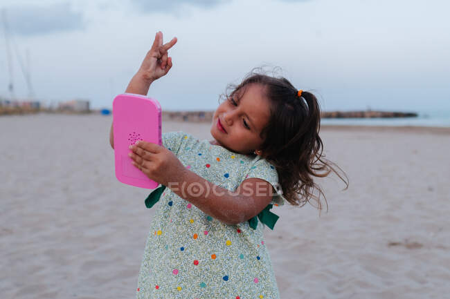 Chica en la playa jugando con el teléfono inteligente rosa - foto de stock