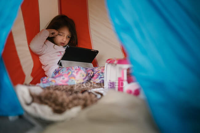 Чотирирічна дівчинка в піжамі дивиться на планшет в маленькому будинку — стокове фото