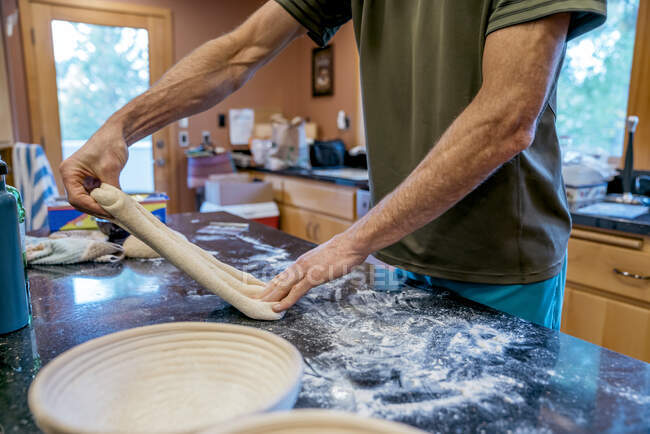 Man stretching sourdough bread dough in messy kitchen — Stock Photo