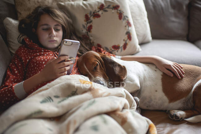 Schönes Mädchen mit Smartphone entspannt sich im Bett mit ihrem Hund — Stockfoto