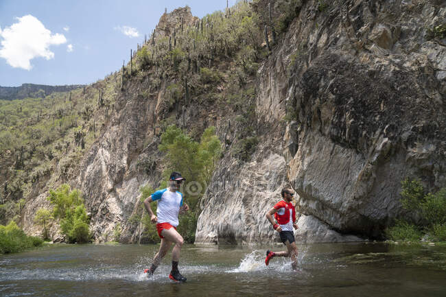 Two men running across a river at the bottom of a canyon in Mexico — Stock Photo