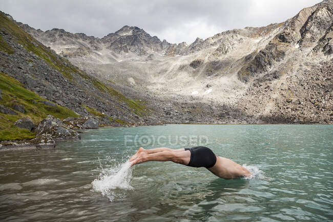 Un uomo si tuffa nel lago superiore della canna per una nuotata, montagne di Talkeetna, Alaska. — Foto stock