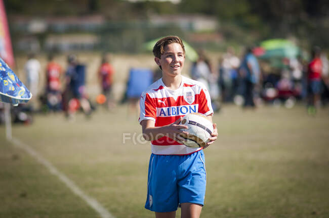 Jugador de fútbol adolescente sonriendo, sosteniendo la pelota y listo para un lanzamiento - foto de stock