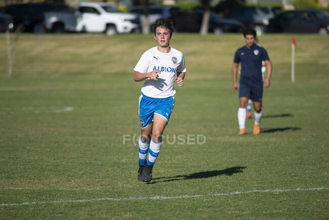 Adolescente jogador de futebol jogging no campo durante um jogo — Fotografia de Stock