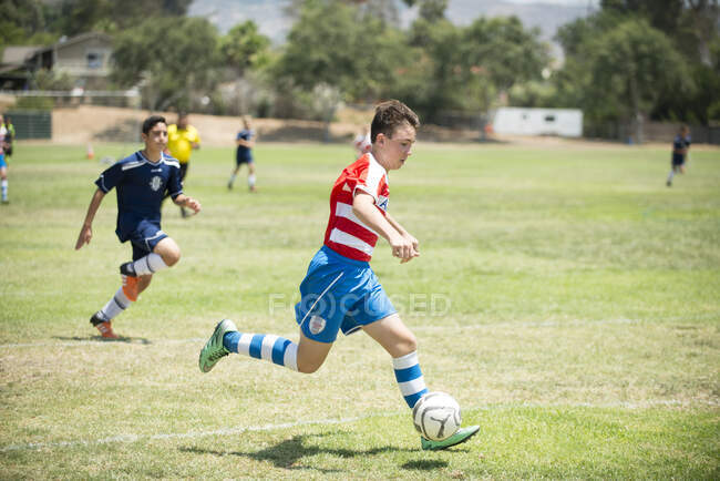 Юный футболист капает мяч во время игры — стоковое фото