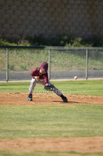 Little League beisebol menino faltando uma bola de chão no campo interno — Fotografia de Stock