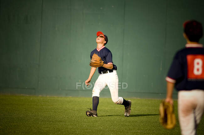 Joven jugador de béisbol en gafas de sol mirando una pelota mosca - foto de stock