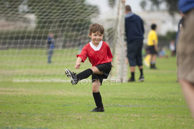 Jovem com grande sorriso chutando uma bola de futebol imaginária — Fotografia de Stock