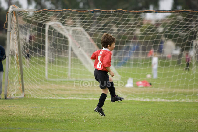 Giovane ragazzo che salta davanti alla porta su un campo da calcio — Foto stock