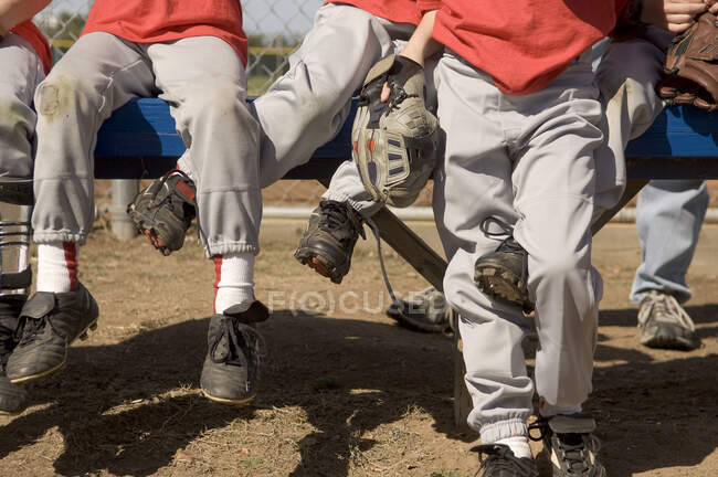 Pernas de meninos entrelaçadas em um banco de beisebol — Fotografia de Stock