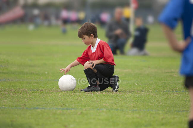 Молодий хлопчик торкається футбольного м'яча пальцем на футбольному полі — стокове фото
