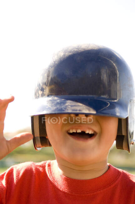 Portrait of young boy missing a tooth with baseball helmet pulled down over his eyes — Stock Photo