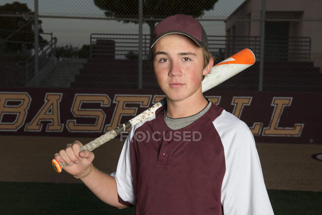 Portrait of a High School baseball player in maroon uniform holding his bat — Stock Photo