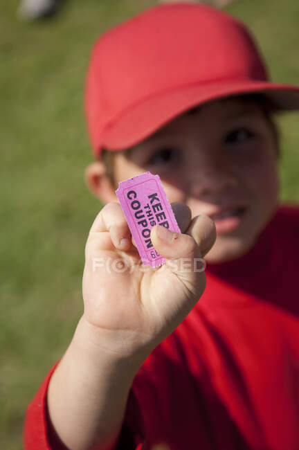 Young boy holding his coupon for the snack shack after his little league game — Stock Photo