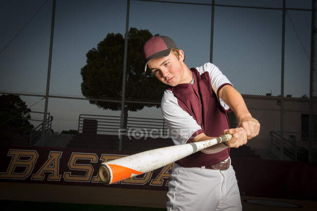 Retrato de un jugador de béisbol de la escuela secundaria en uniforme granate balancear su bate - foto de stock