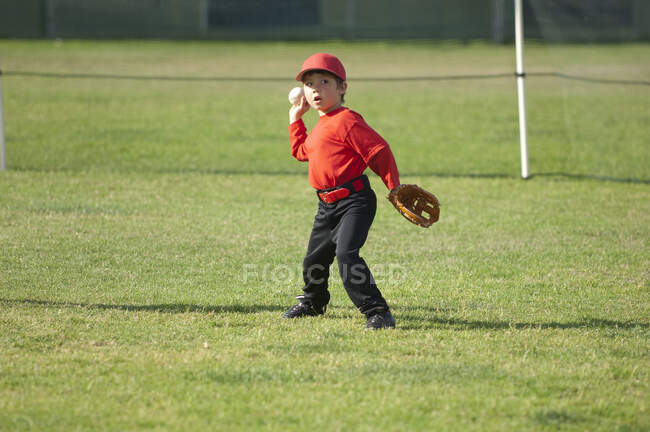Niño lanzando una pelota de béisbol en el campo de béisbol - foto de stock