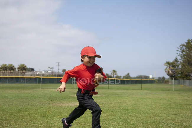 Niño sosteniendo su guante y corriendo a través del campo de pelota - foto de stock