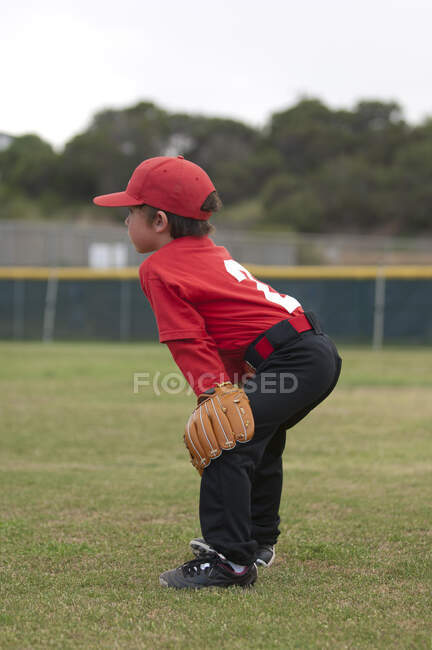 Jeune garçon avec ses mains et son gant sur ses quilles sur un terrain de baseball — Photo de stock