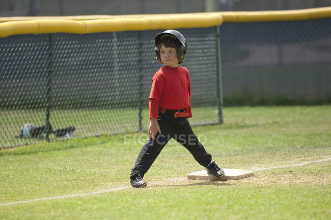 Niño sonriendo en tercera base en el campo de béisbol - foto de stock