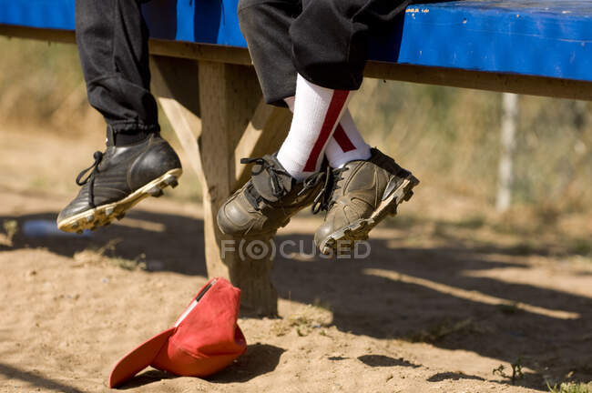 Gambe di 2 ragazzi seduti sulla panchina di una panchina di baseball — Foto stock