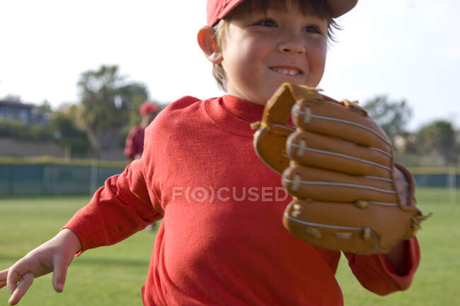 Gros plan sur un jeune garçon fuyant les champs de TBall avec un grand sourire — Photo de stock