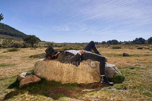 Молодий татуйований чоловік лежить на скелі в сільській місцевості — стокове фото