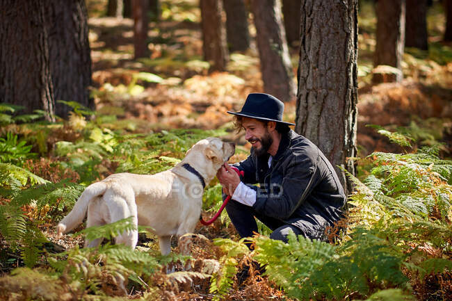 Retrato del joven hombre tatuado con su perro en el bosque - foto de stock