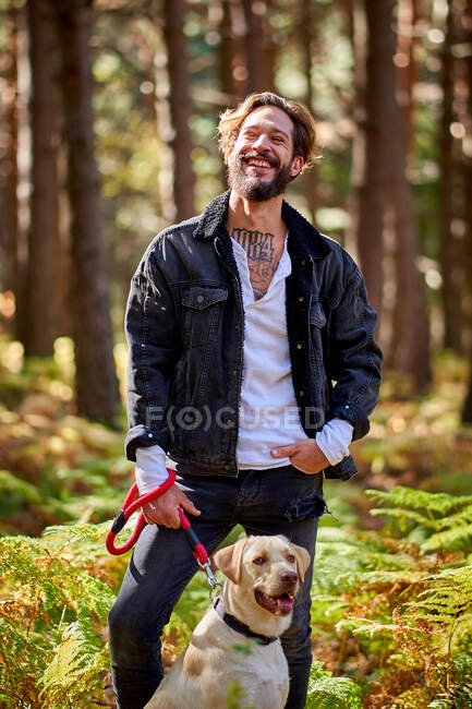 Retrato del joven hombre tatuado con su perro en el bosque - foto de stock