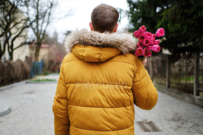 Blond man in a yellow winter jacket with a bouquet of tulips in hands — Stock Photo