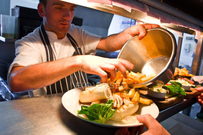Chef adds french fries to a dish at commercial kitchen — Stock Photo