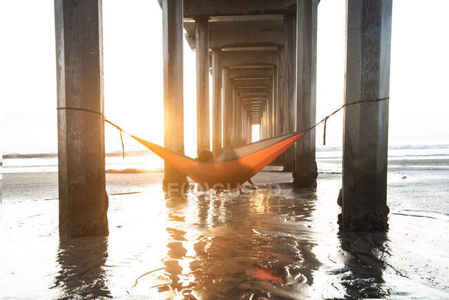 Girls in a hammock under a pier by the ocean at sunset — Stock Photo
