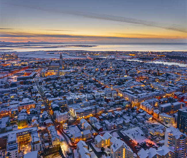Impresionante vista de drones de edificios residenciales iluminados con techos nevados ubicados en las calles de la ciudad costera durante la puesta del sol en Islandia - foto de stock