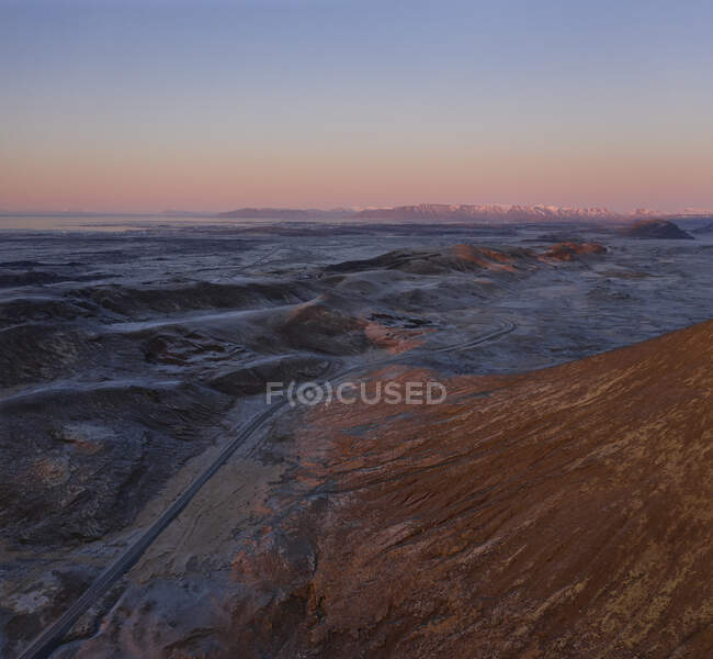 Desde arriba pintoresco paisaje nórdico con camino de asfalto vacío que pasa por un terreno volcánico rocoso bajo el cielo sin nubes puesta de sol en Islandia - foto de stock
