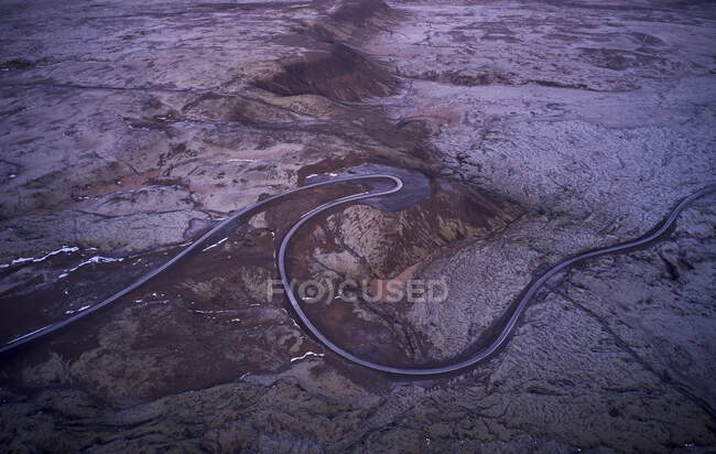 Drone view of narrow winding asphalt road running through rough desert rocky terrain in Iceland — Stock Photo