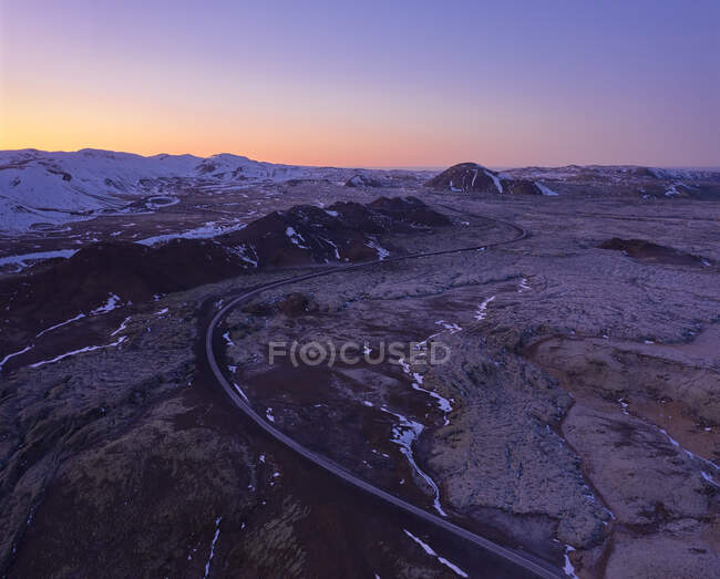 Сверху пустого извилистого шоссе, проходящего по пересеченной горной местности Исландии на закате солнца с красивым красочным небом — стоковое фото