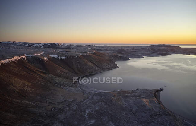 Maravilloso paisaje de puesta de sol de la costa rocosa áspera con agua tranquila contra el cielo colorido sin nubes en Islandia - foto de stock