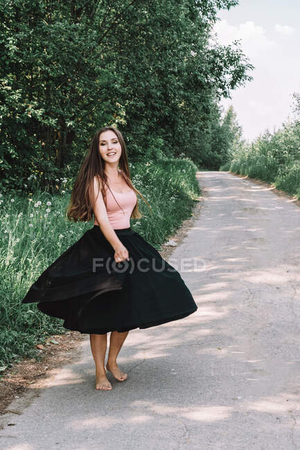 Красивая девушка в полной юбке танцует на дороге — стоковое фото