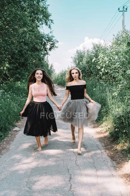 Deux belles filles en jupes pleines courent le long de la route — Photo de stock