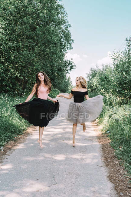 Dos hermosas chicas en faldas completas bailando en la carretera - foto de stock