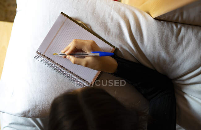 Mulher deitada na cama escrevendo em seu livro de datas. — Fotografia de Stock