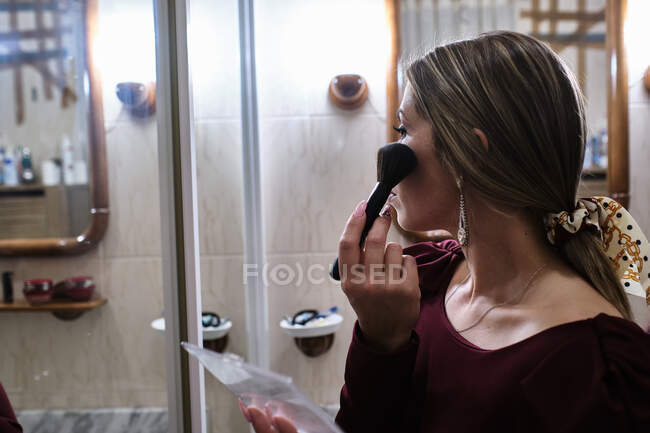 Jeune femme se maquille dans la salle de bain en regardant dans le miroir — Photo de stock