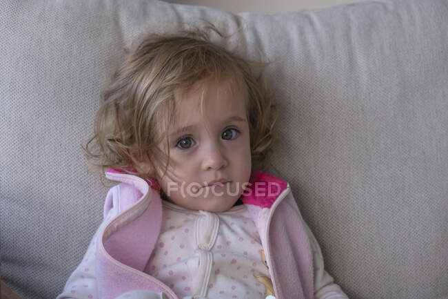 Маленька дівчинка дивиться на камеру, сидячи на дивані — стокове фото