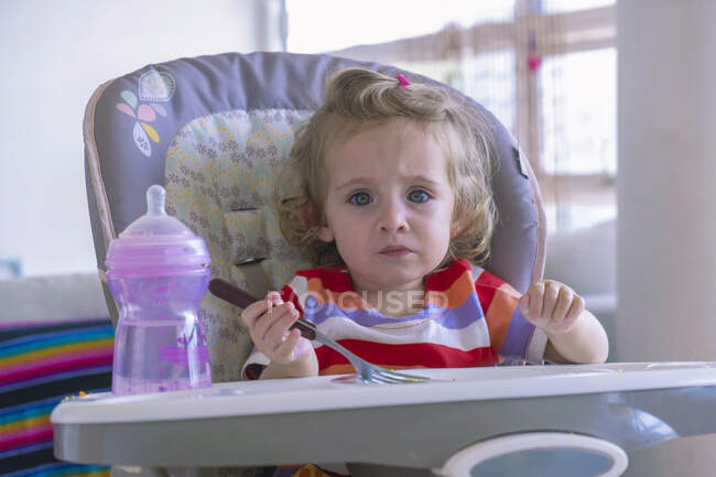Kleines Mädchen füttert allein in ihrem Stuhl im Wohnzimmer. — Stockfoto