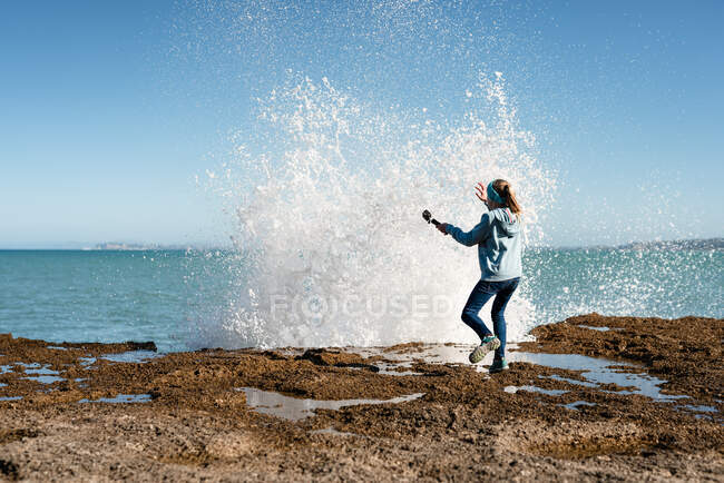 Tween assustado pela onda batendo sobre a rocha — Fotografia de Stock