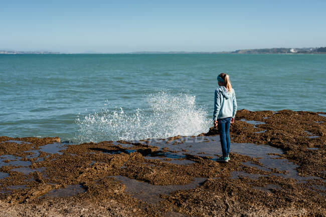 Девочка-подросток смотрит, как волны льются над камнями в Новой Зеландии — стоковое фото