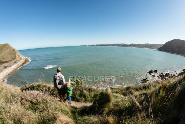 Father and young child looking down at ocean from mountain trail — Stock Photo